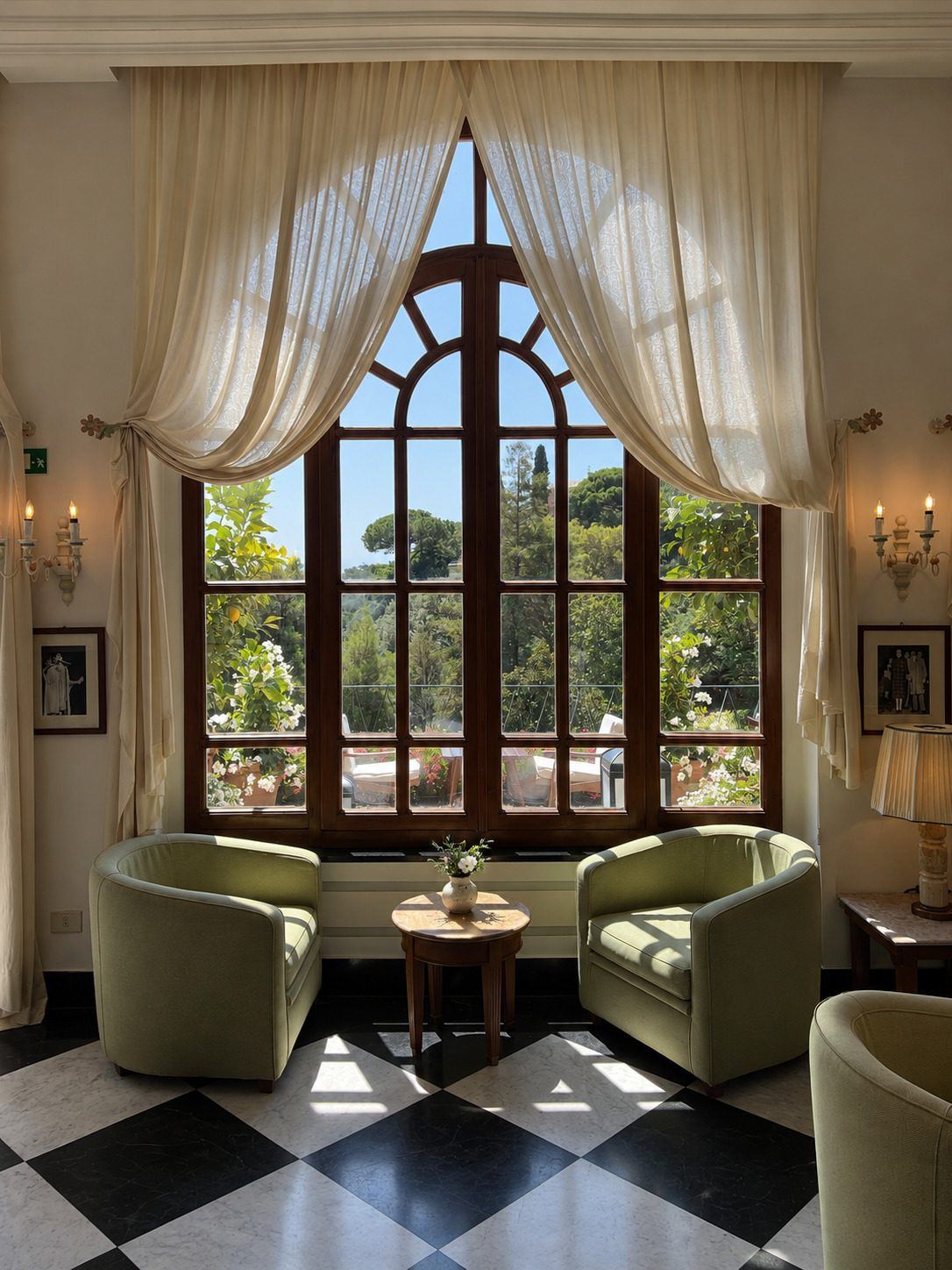 Dos sillones verdes junto a un ventanal en arco con cortinas claras y vista a un jardín.